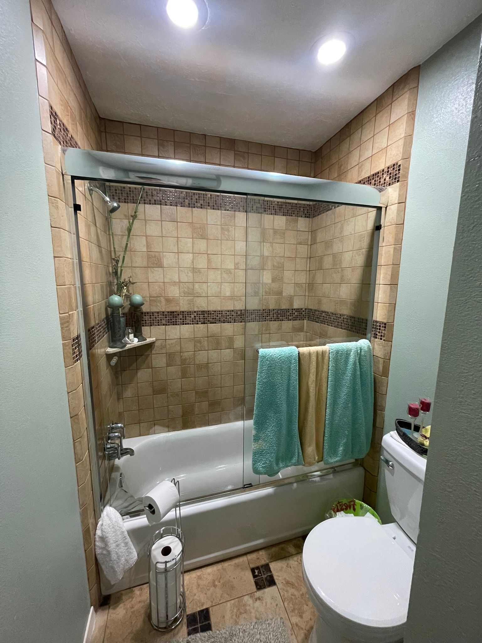 A bathroom with a bathtub, sliding glass shower doors, tan tiled walls, light green walls, and a white toilet.