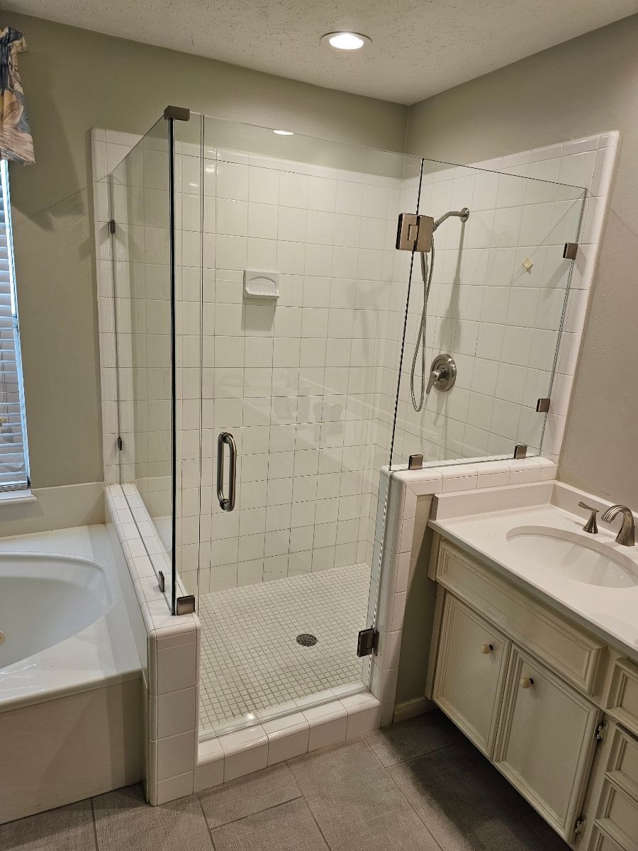 A walk-in shower with a glass door and walls, featuring white tiled walls, a penny-tiled floor, and a metal shower head.