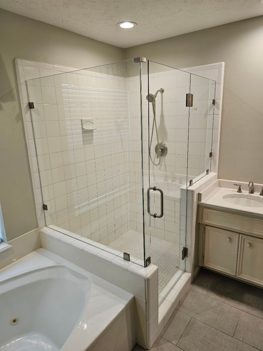 A glass-enclosed shower with white tiled walls, positioned next to a bathtub and a vanity in a bathroom.