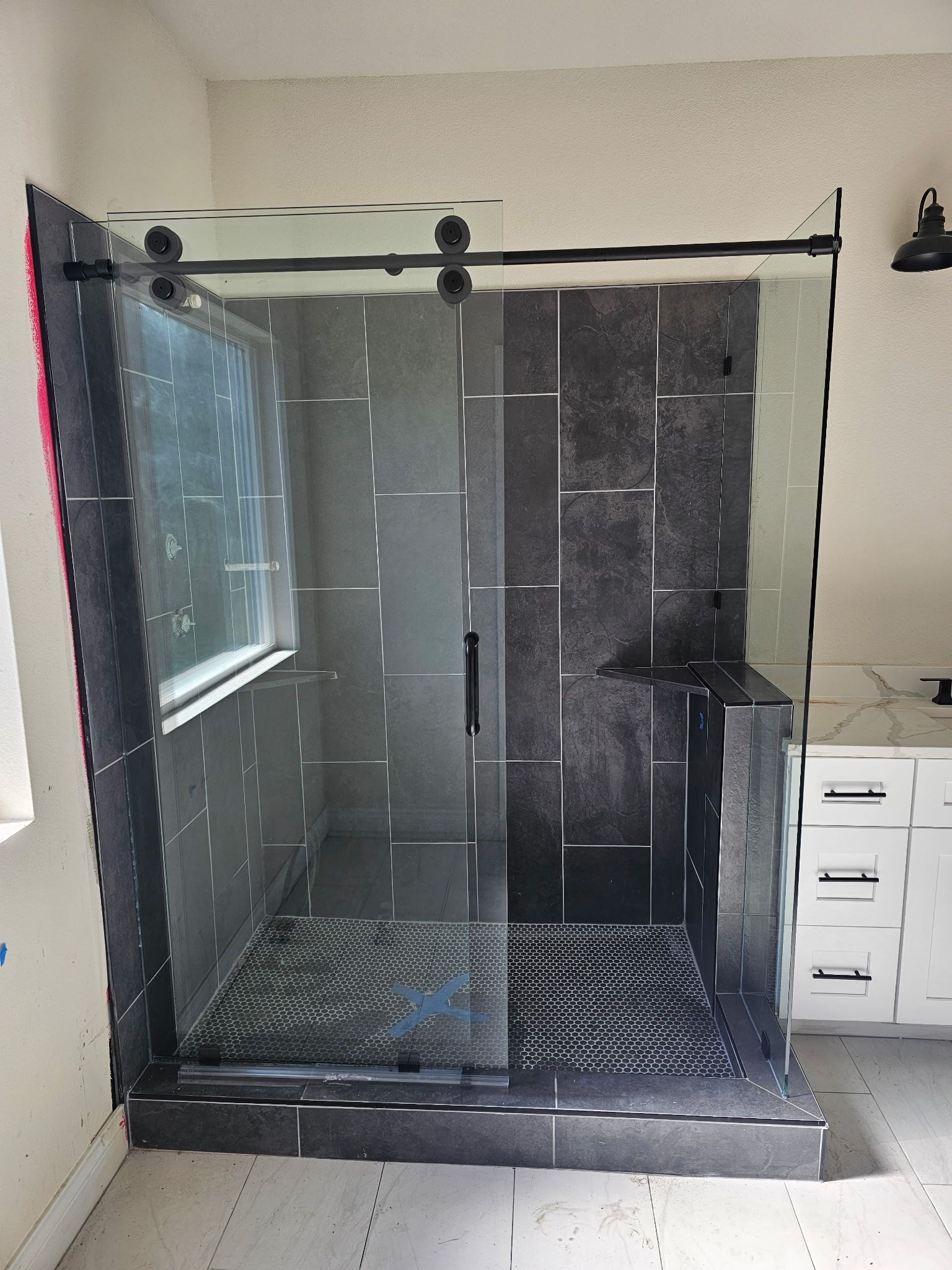 A modern glass shower enclosure with black hardware and dark grey, vertically installed tiled walls.
