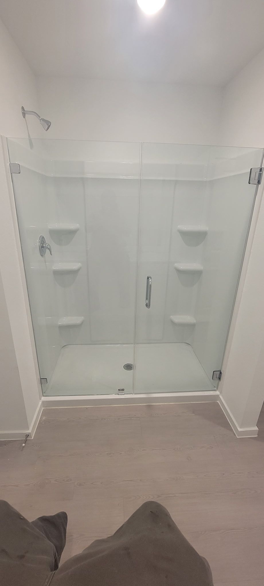 A modern white shower stall with glass doors, built-in corner shelves, and a single shower head.