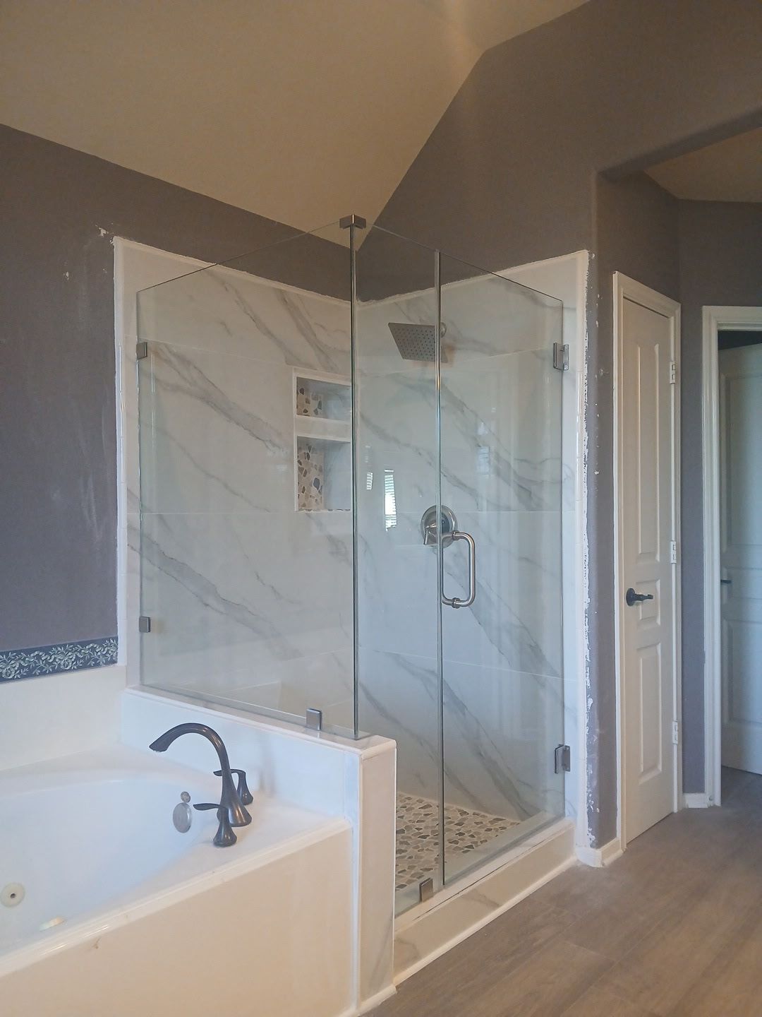 A walk-in shower with a glass door and marble-look tiles, situated next to a soaking tub in a modern bathroom.
