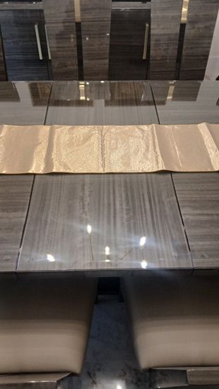 A polished grey wood dining table with a gold runner, surrounded by chairs with beige seats.