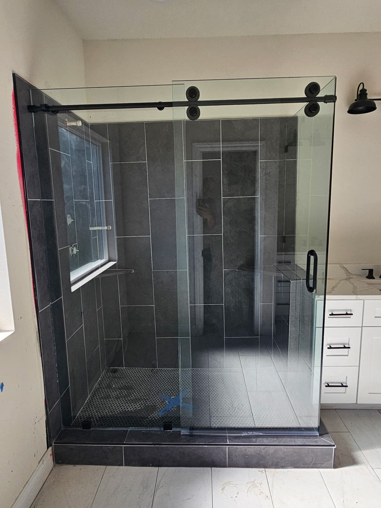 A glass sliding shower door with matte black hardware installed on a tiled shower curb in a bathroom.