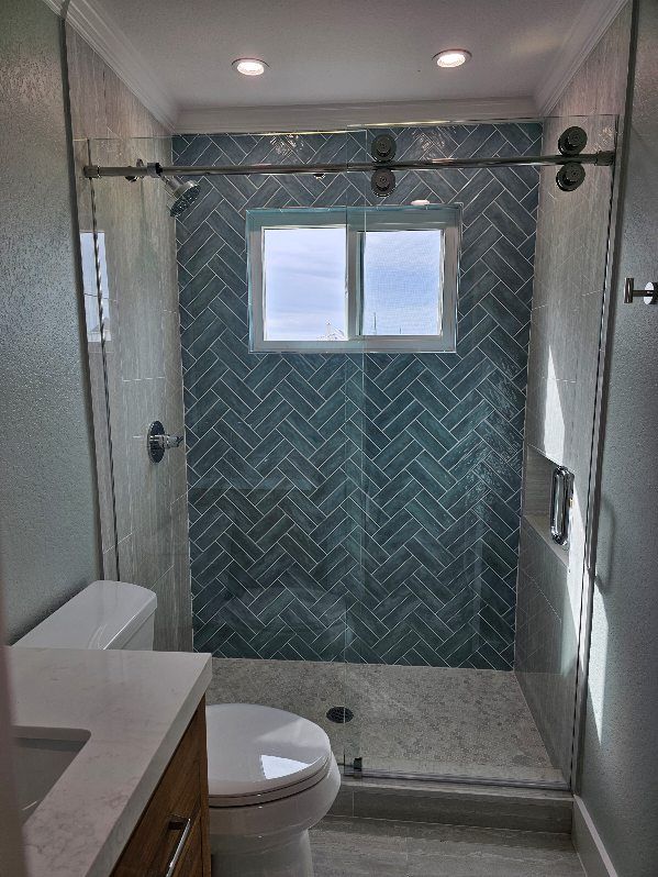 A bathroom featuring a walk-in shower with blue herringbone tiles, a sliding glass door, and a white vanity and toilet.