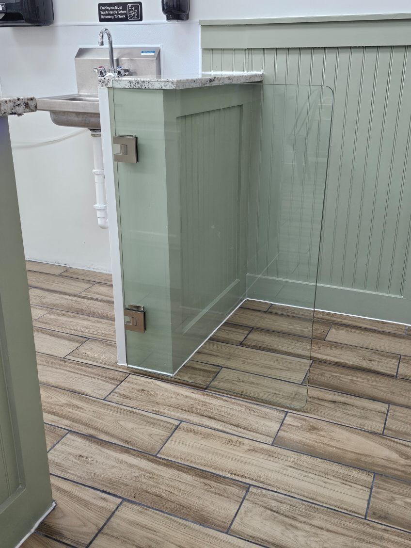 A view of a public restroom with a sage green paneled partition wall and wood-look tile flooring leading to a sink.