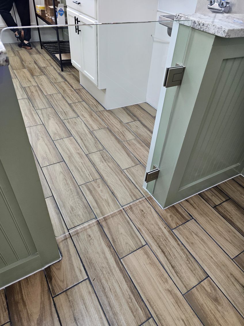 A metal safety gate installed between a sage green cabinet and a wall over wood-look tile flooring.