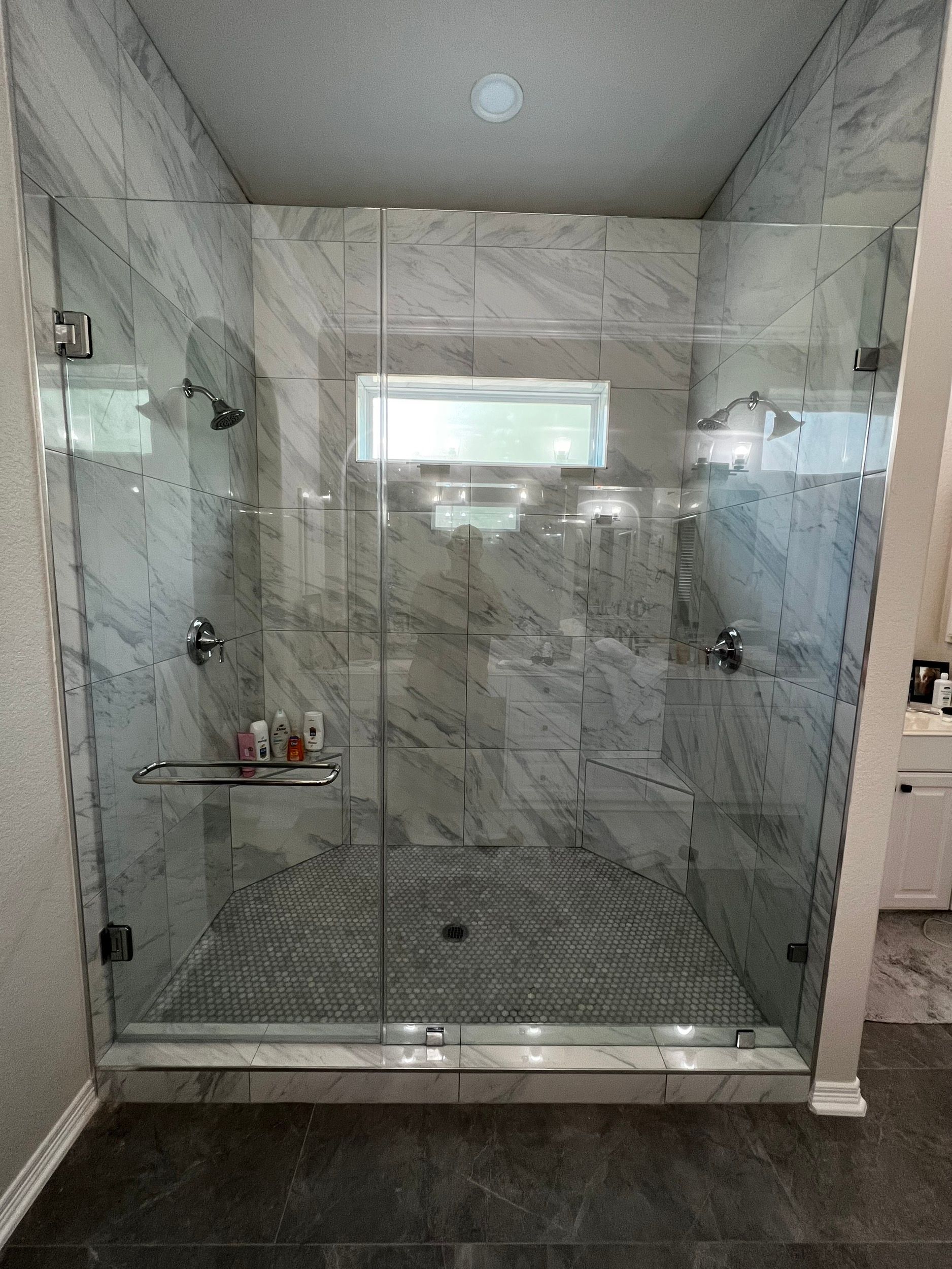 A modern walk-in shower with clear glass doors, marble-patterned tile walls, and a dark mosaic-tiled floor.