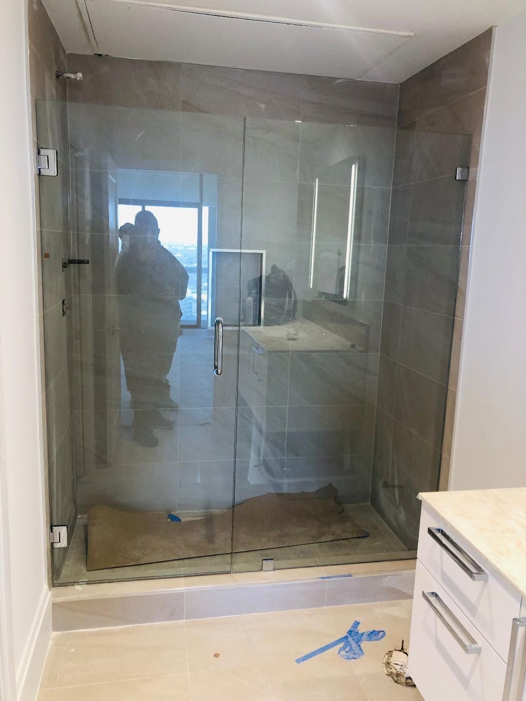 A glass shower enclosure with a door, installed in a bathroom with beige tiled walls and a light floor.