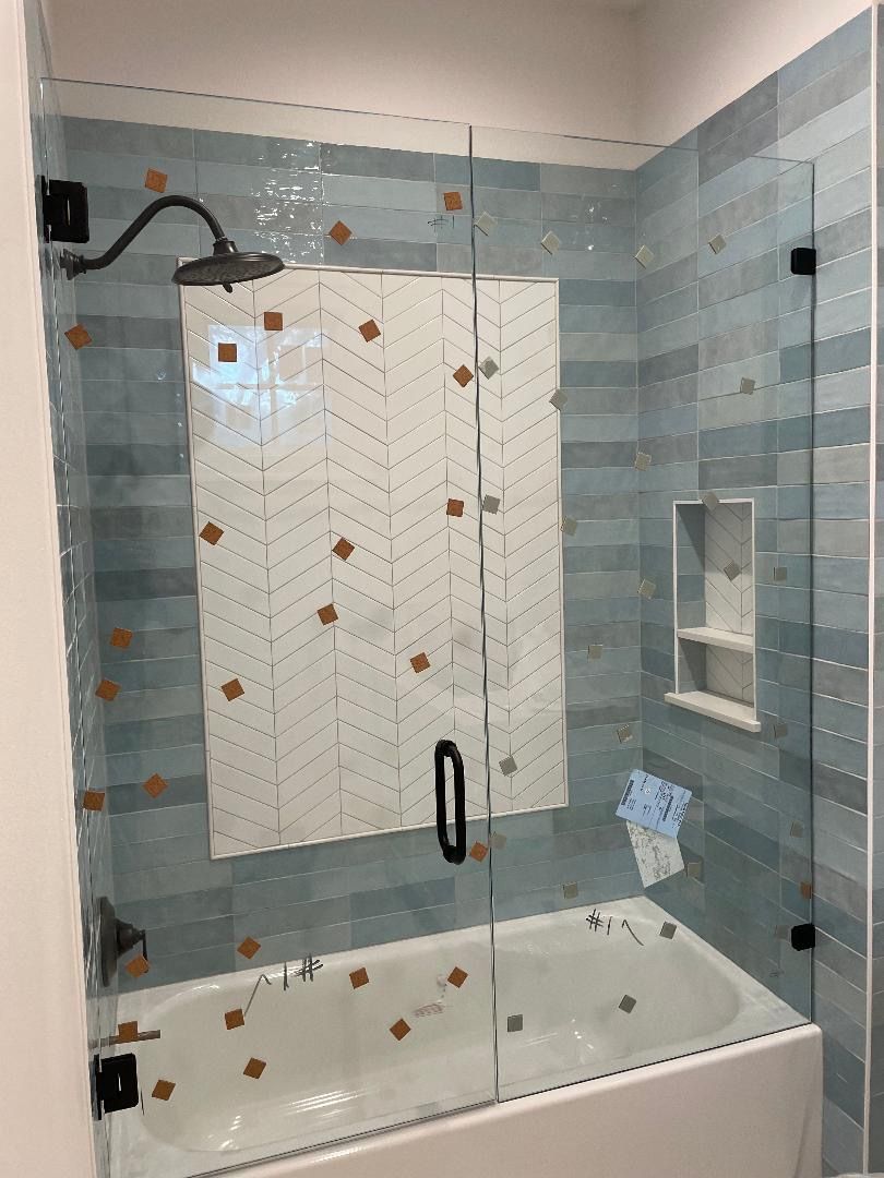 A bathtub with a glass door, featuring blue tiled walls and a white chevron-patterned accent wall with copper accents.