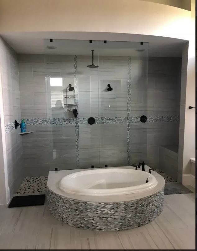 A bathroom featuring a circular jetted tub with mosaic tile accents, set in front of a walk-in shower with glass doors.