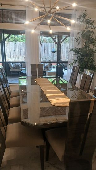 A dining room with a long glass table, tall gray chairs, and a modern sputnik chandelier in front of a sunroom window.