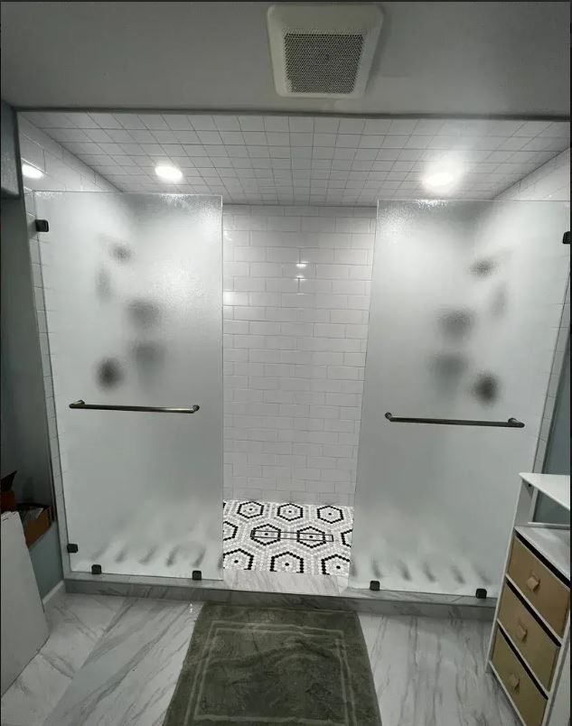 A double-door glass shower with frosted panels, white subway tile walls, and a patterned hexagonal floor tile.