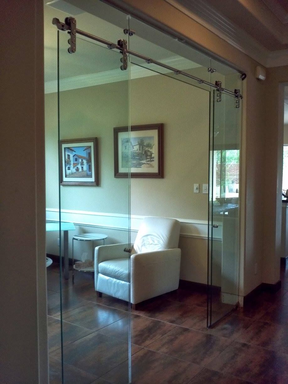 A sliding glass door with metallic hardware, separating a hallway from a room containing a white chair and wall art.