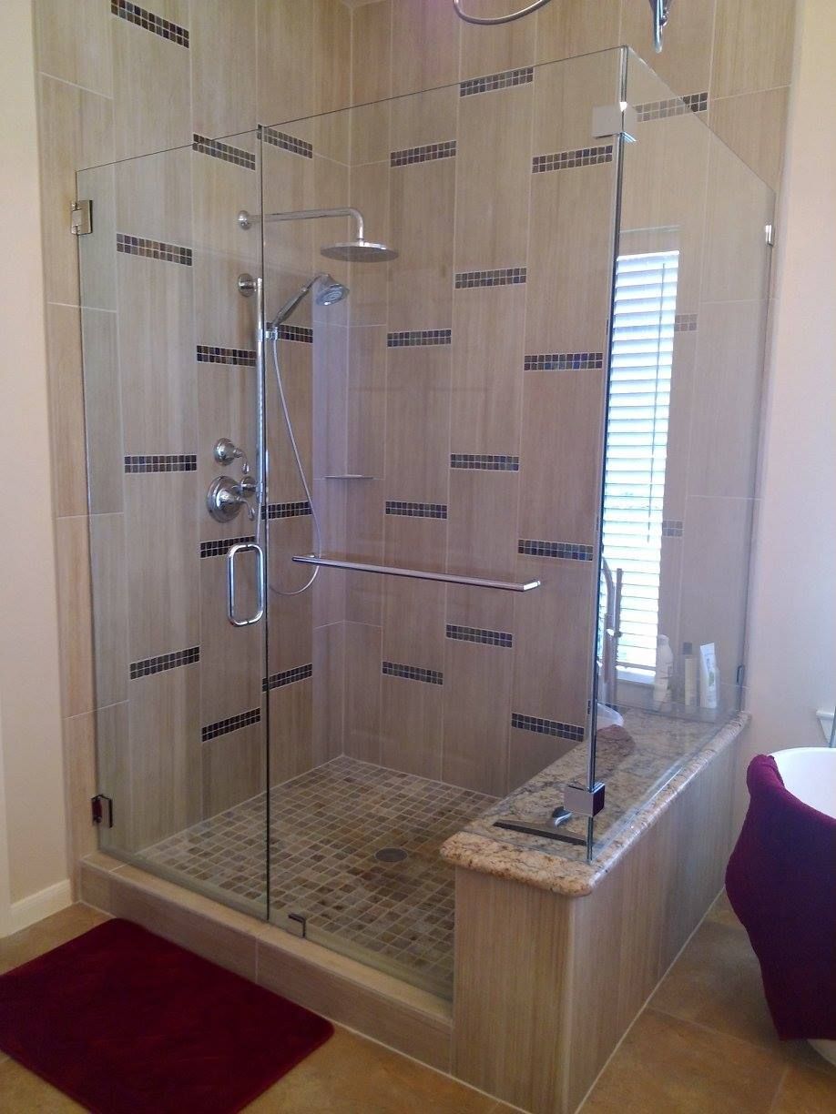 A glass-enclosed shower with beige tile walls, a stone bench, and a rainfall showerhead in a modern bathroom.