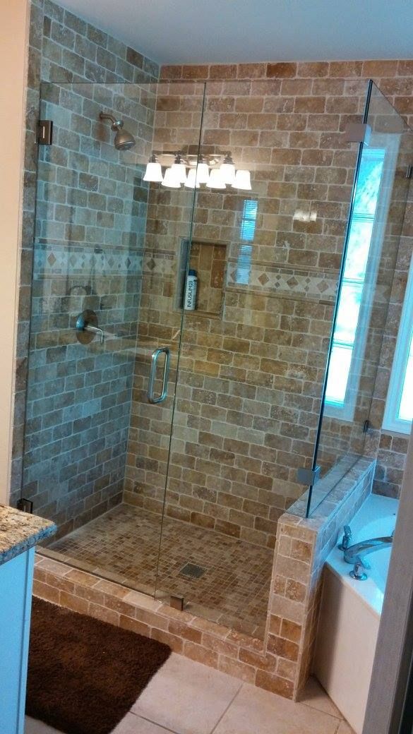A glass-enclosed shower with beige brick walls and flooring, featuring a built-in shampoo niche and overhead lighting.