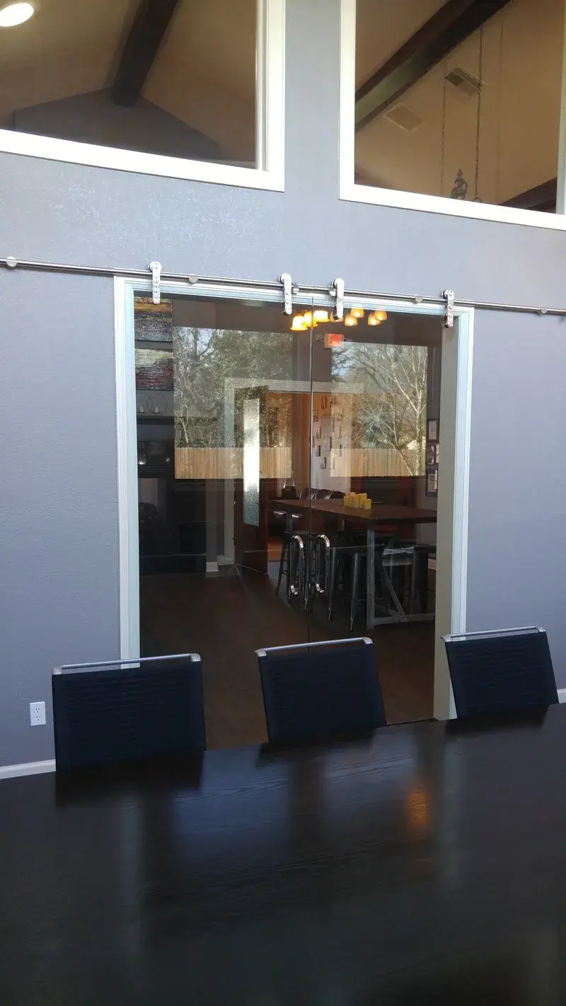 A sliding glass barn door mounted on a track in a gray wall, revealing a dining area with a table and stools inside.