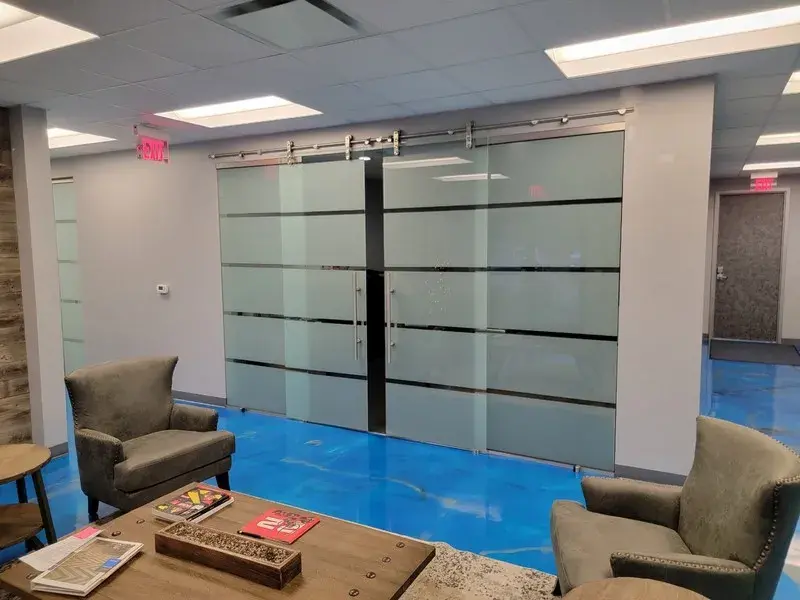Modern lobby with two gray chairs, a wooden coffee table, and large sliding glass office doors with horizontal stripes.