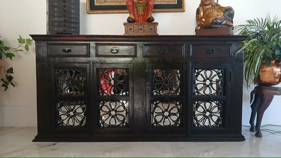 A dark wooden sideboard with four drawers above four cabinet doors featuring decorative black iron floral grilles.