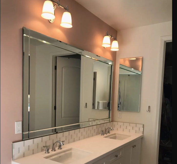 A double vanity with white sinks, quartz countertops, a large mirror, two vanity light fixtures, and a dusty pink wall.