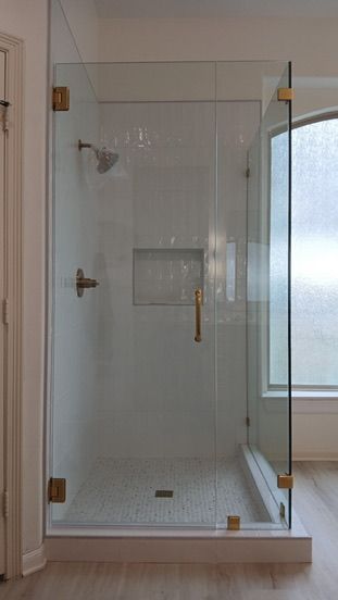 A glass shower enclosure with gold-tone hardware and a tiled floor in a bathroom.