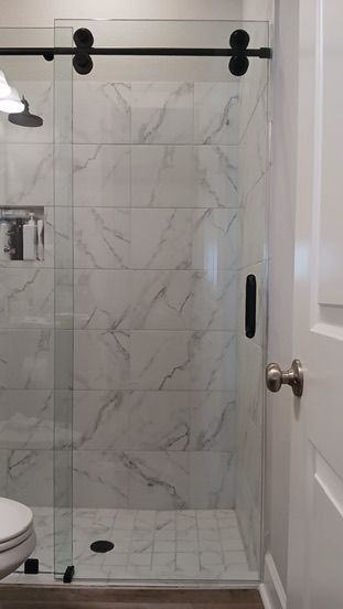 A glass shower stall with black hardware and a sliding door, set against marble-patterned tile walls.