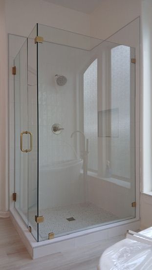 A glass shower enclosure with gold-tone hardware and hinges, set in a light-colored bathroom.