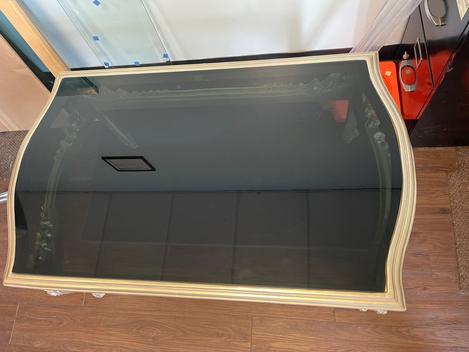 A rectangular coffee table with a dark, reflective glass top and an ornate, light-colored, textured frame.