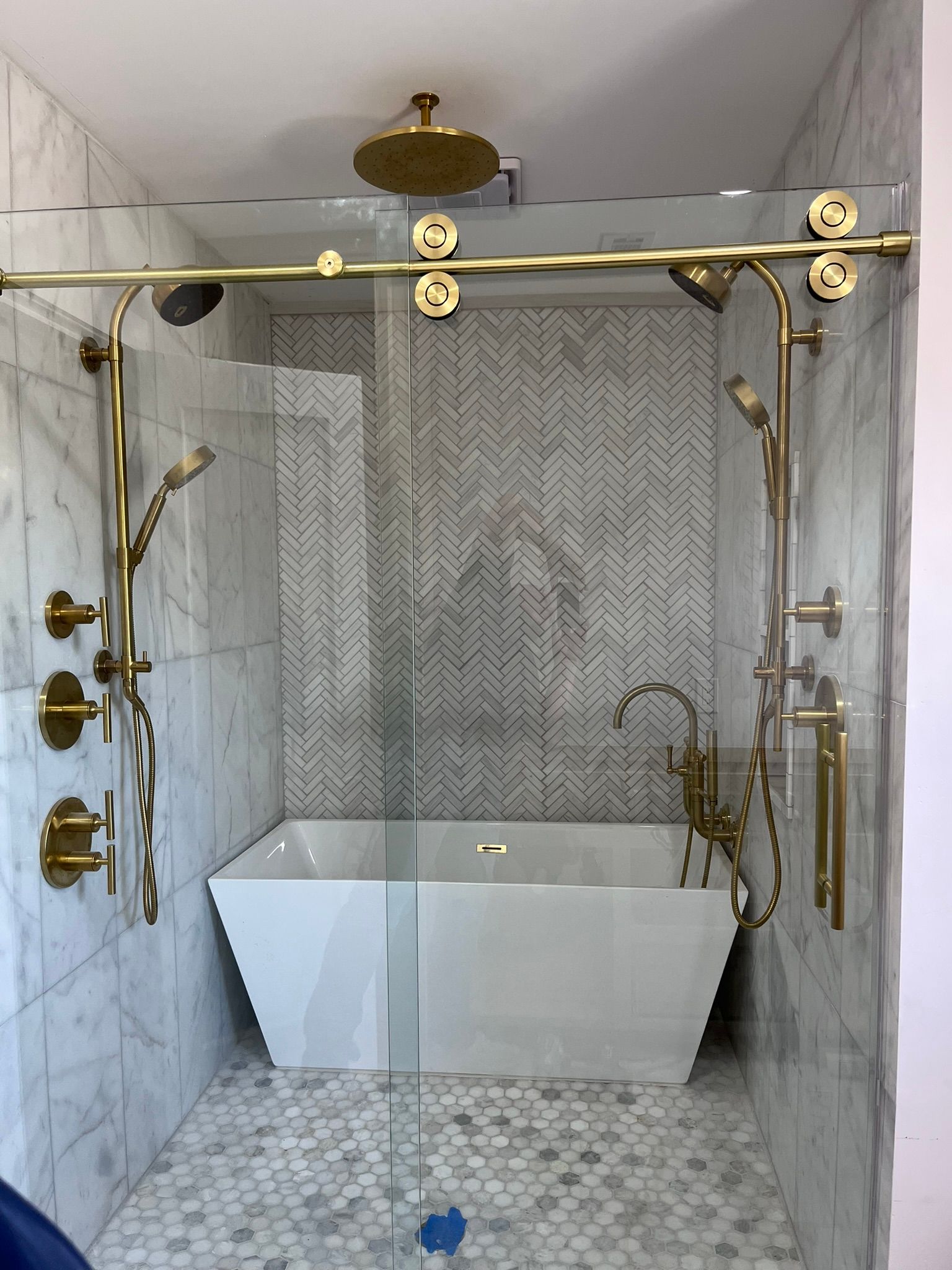 A modern shower and bathtub combination with marble tile walls, a herringbone accent wall, and gold-toned fixtures.