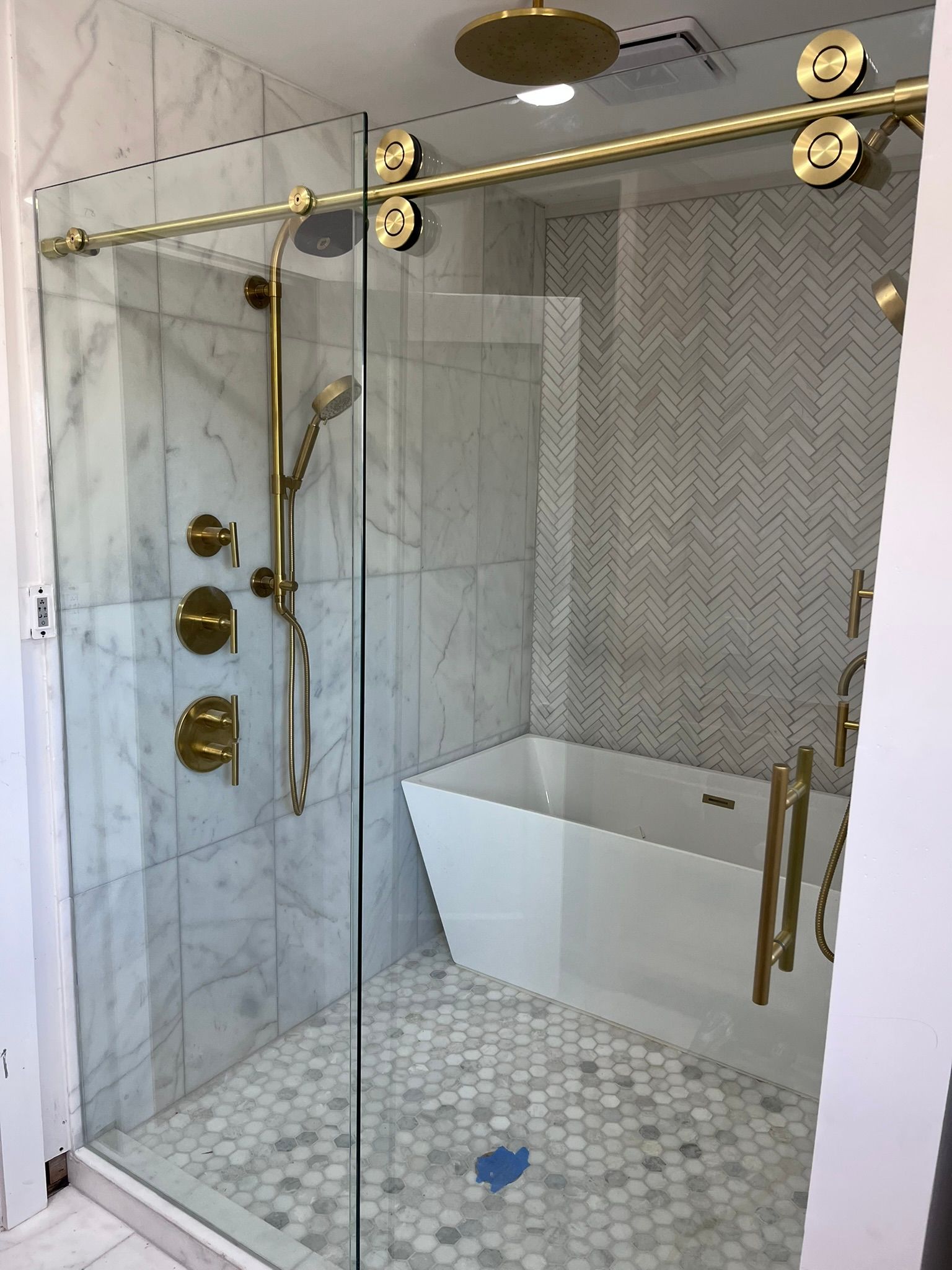 A modern walk-in shower with gold hardware, a glass sliding door, marble tile walls, and a separate white bathtub.