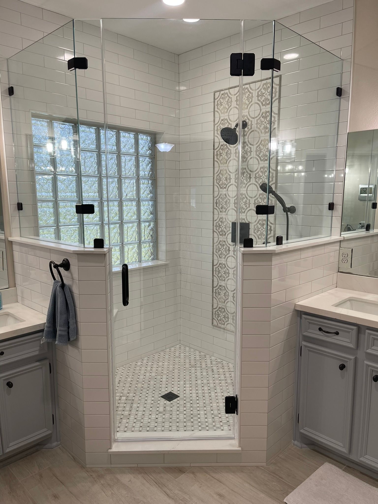 A walk-in shower with glass doors, white tiled walls, a decorative patterned wall, and a frosted glass window.