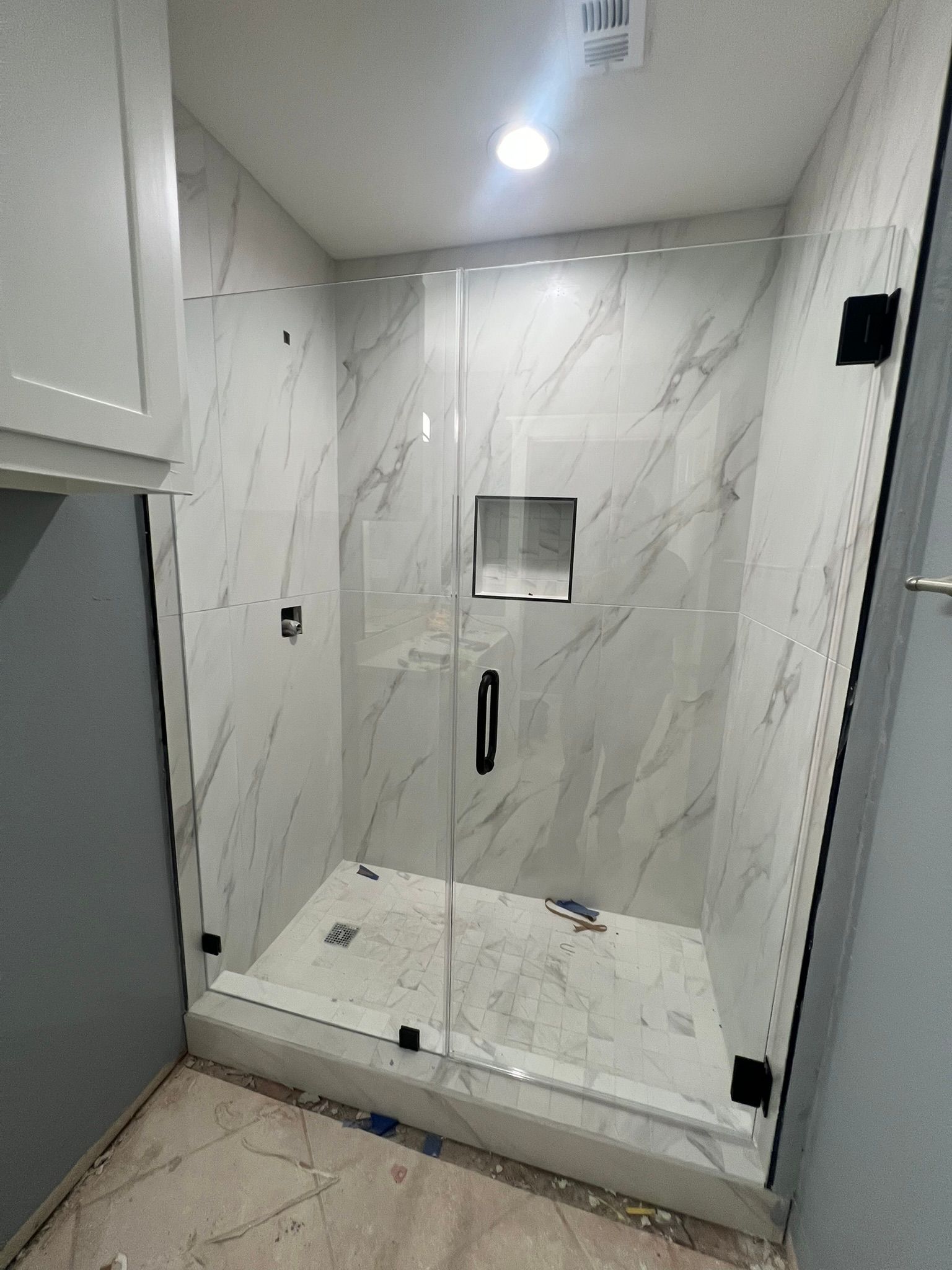 A frameless glass shower enclosure with white marble-patterned tiled walls and floor, featuring a built-in shower niche.