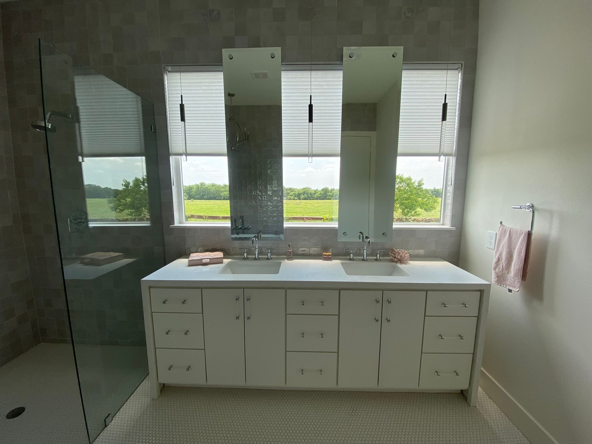 A double bathroom vanity with white cabinets, two rectangular mirrors, dual sinks, and a large window overlooking a field.