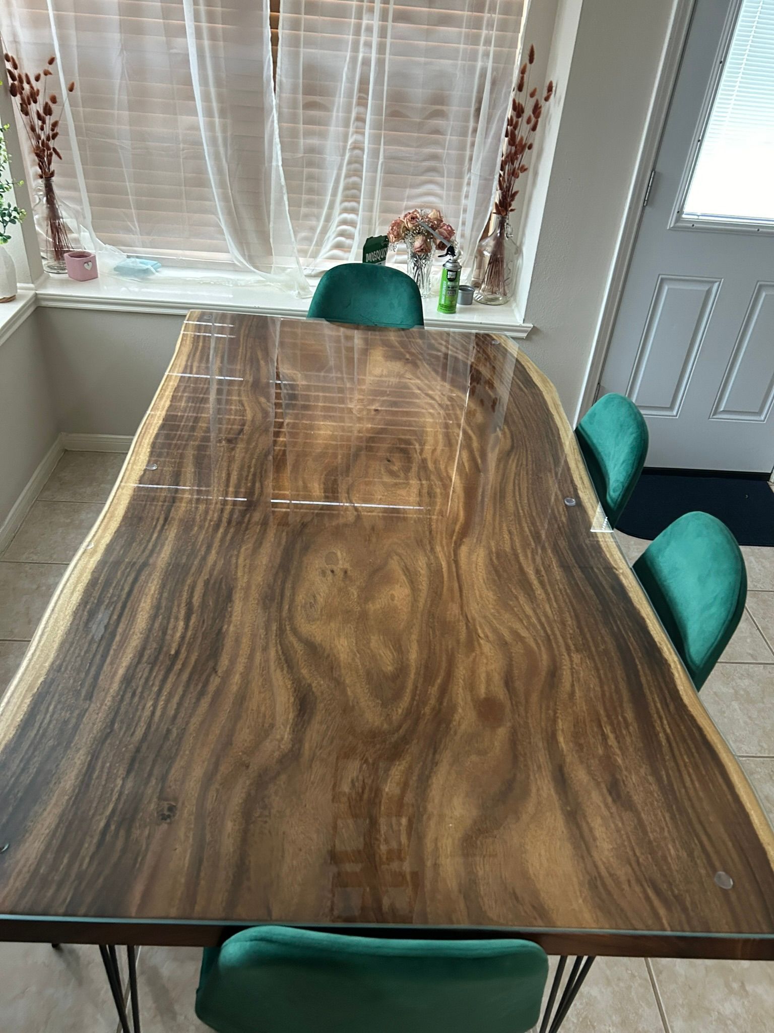 A live-edge wood dining table with a glossy finish and green velvet chairs in a sunlit room.