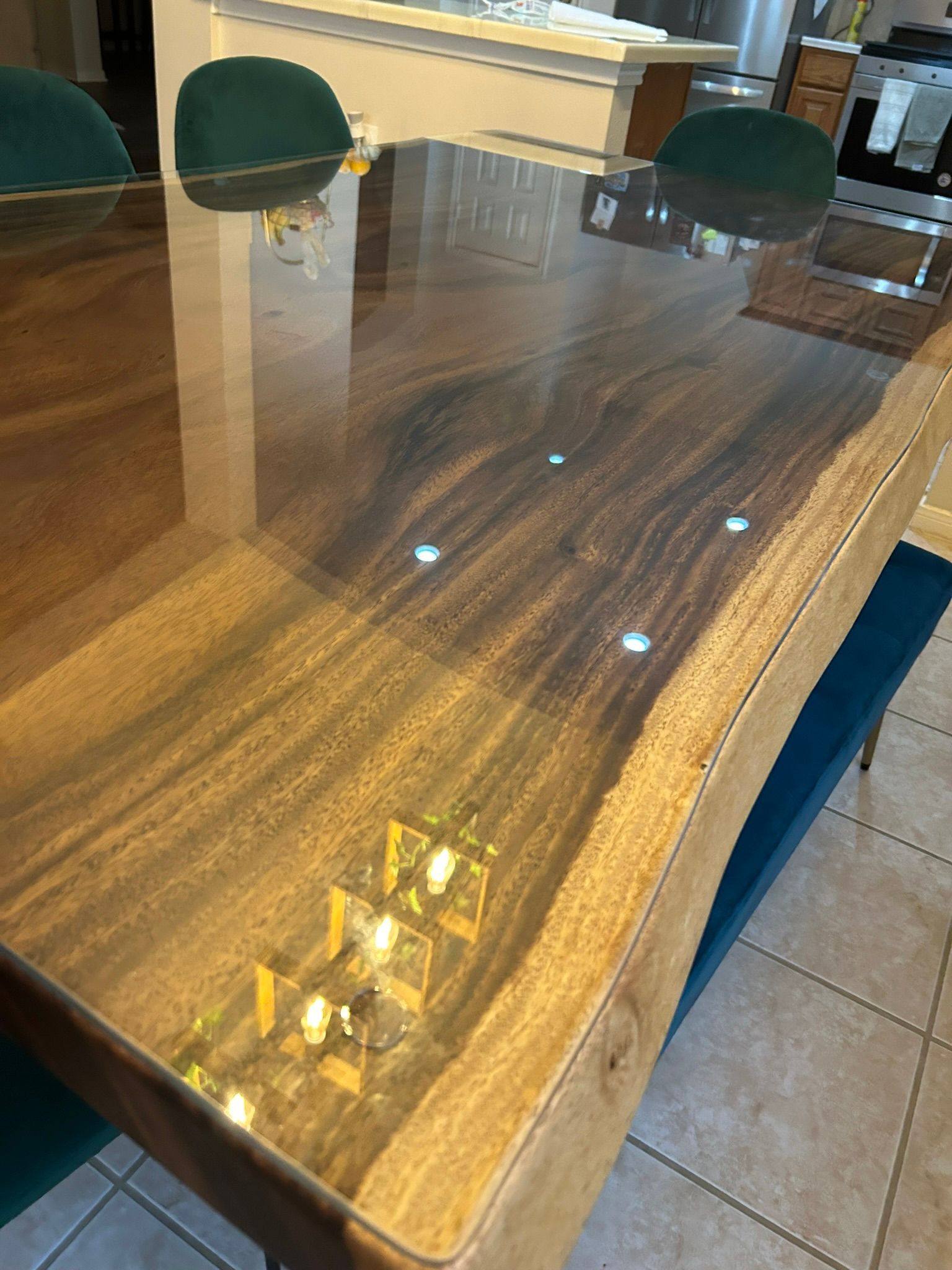 A wooden dining table with a glossy finish and a clear protective cover, surrounded by dark green chairs.