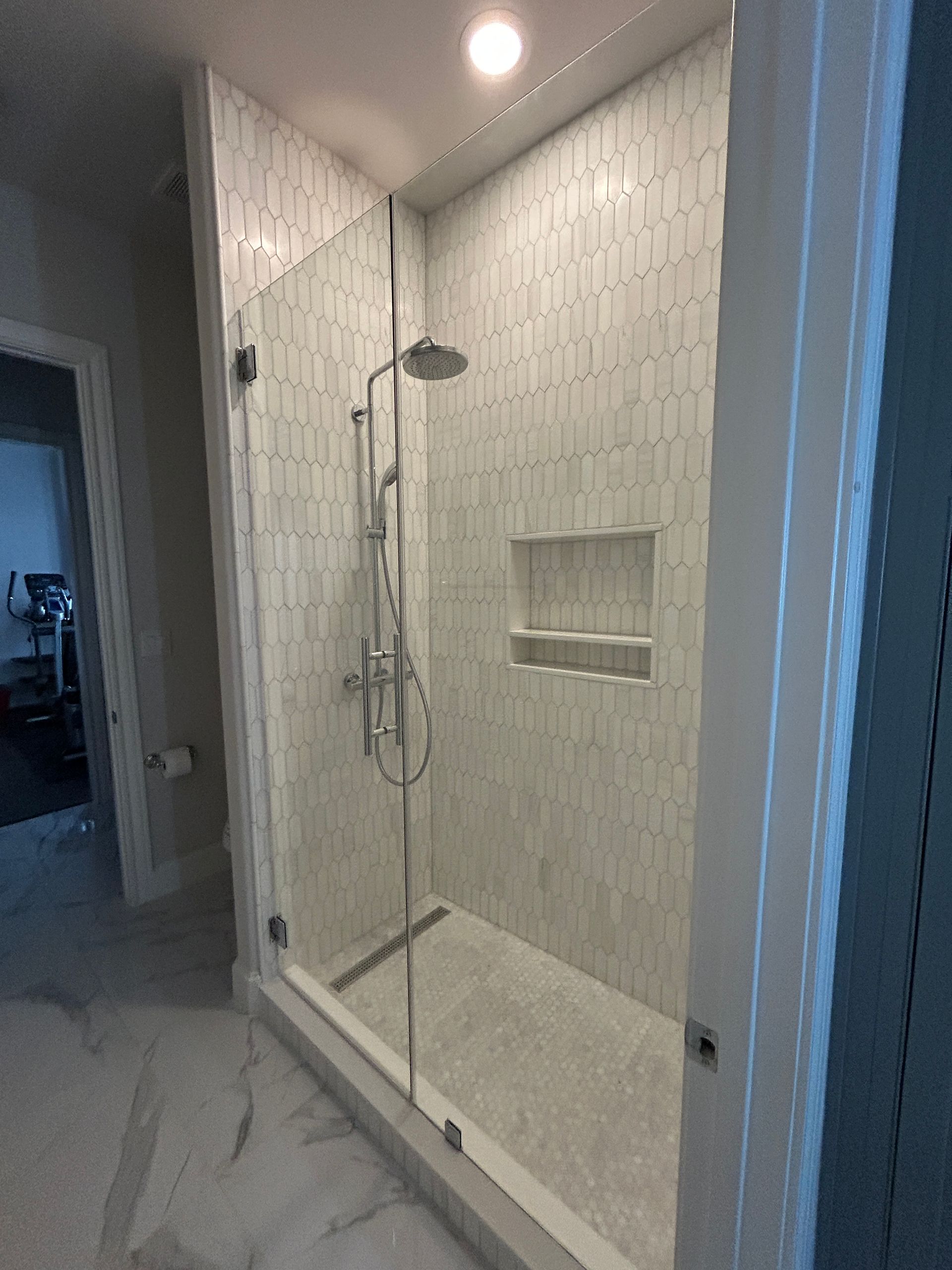 A modern shower with white textured tile walls, a glass door, a built-in niche, and a chrome rainfall showerhead.