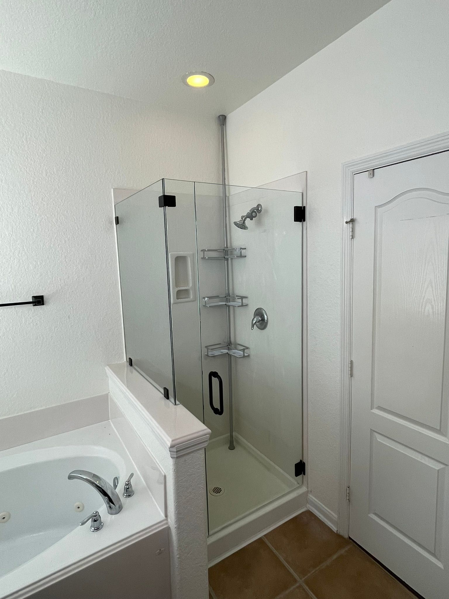 A modern bathroom featuring a white soaking tub next to a corner glass-enclosed shower with metal shelving and tile floor.