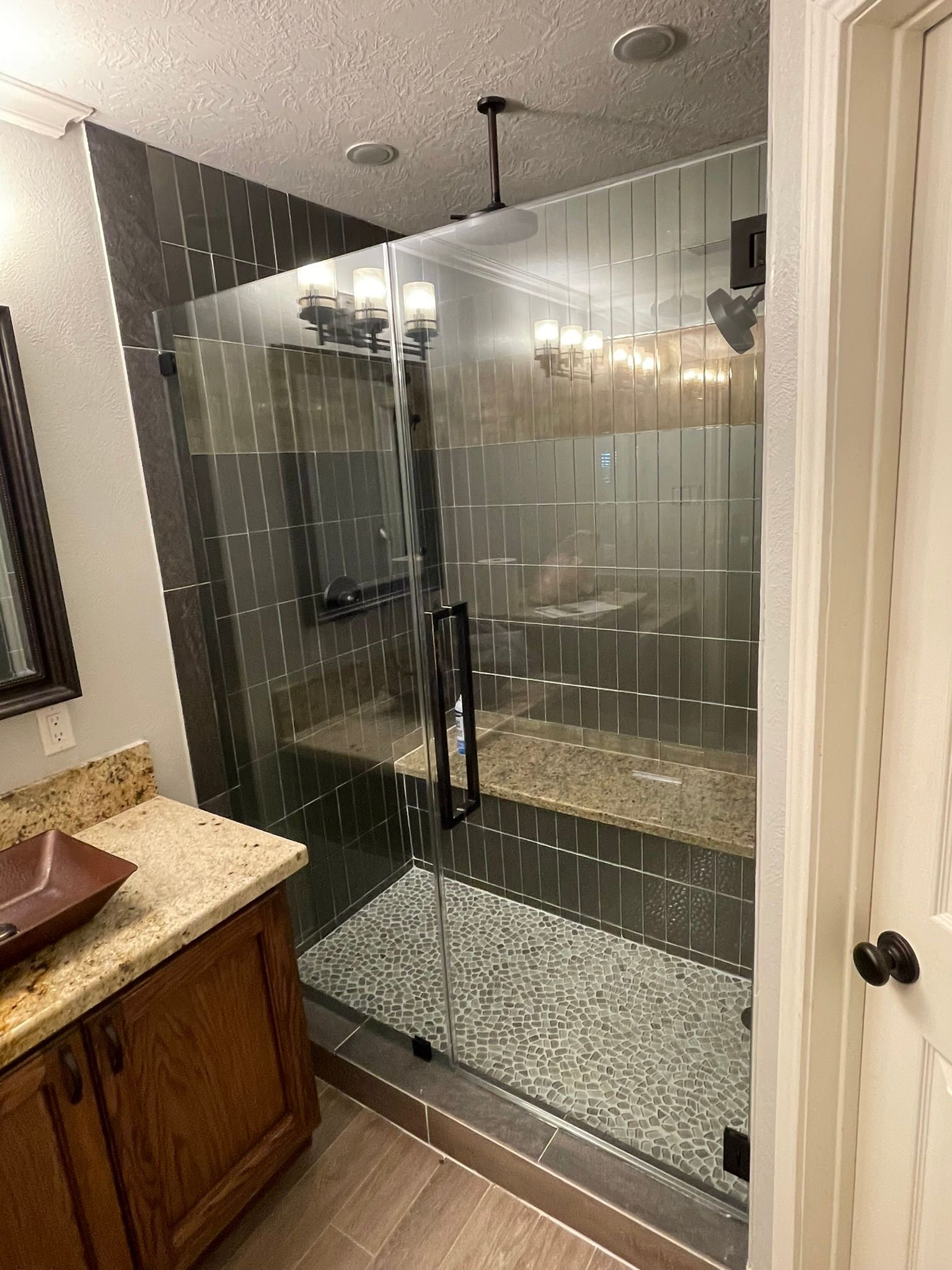 A modern bathroom featuring a glass-enclosed shower with a stone bench and a wooden vanity with a brown countertop.