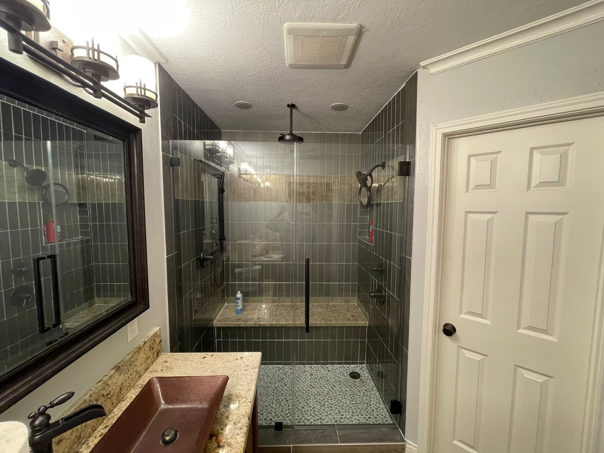 A bathroom vanity with a copper sink and a tiled walk-in shower with a glass door and stone bench.