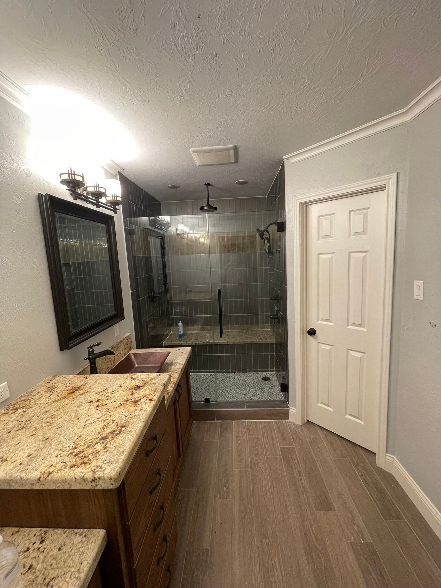 A bathroom featuring a granite vanity, dark wood cabinetry, a glass-enclosed shower, and a white door on a gray wall.