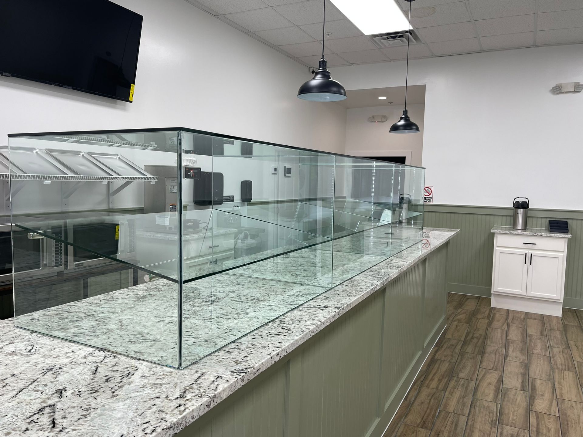 A granite countertop with a long, transparent glass display case in a room with white walls, sage paneling, and pendant lights.