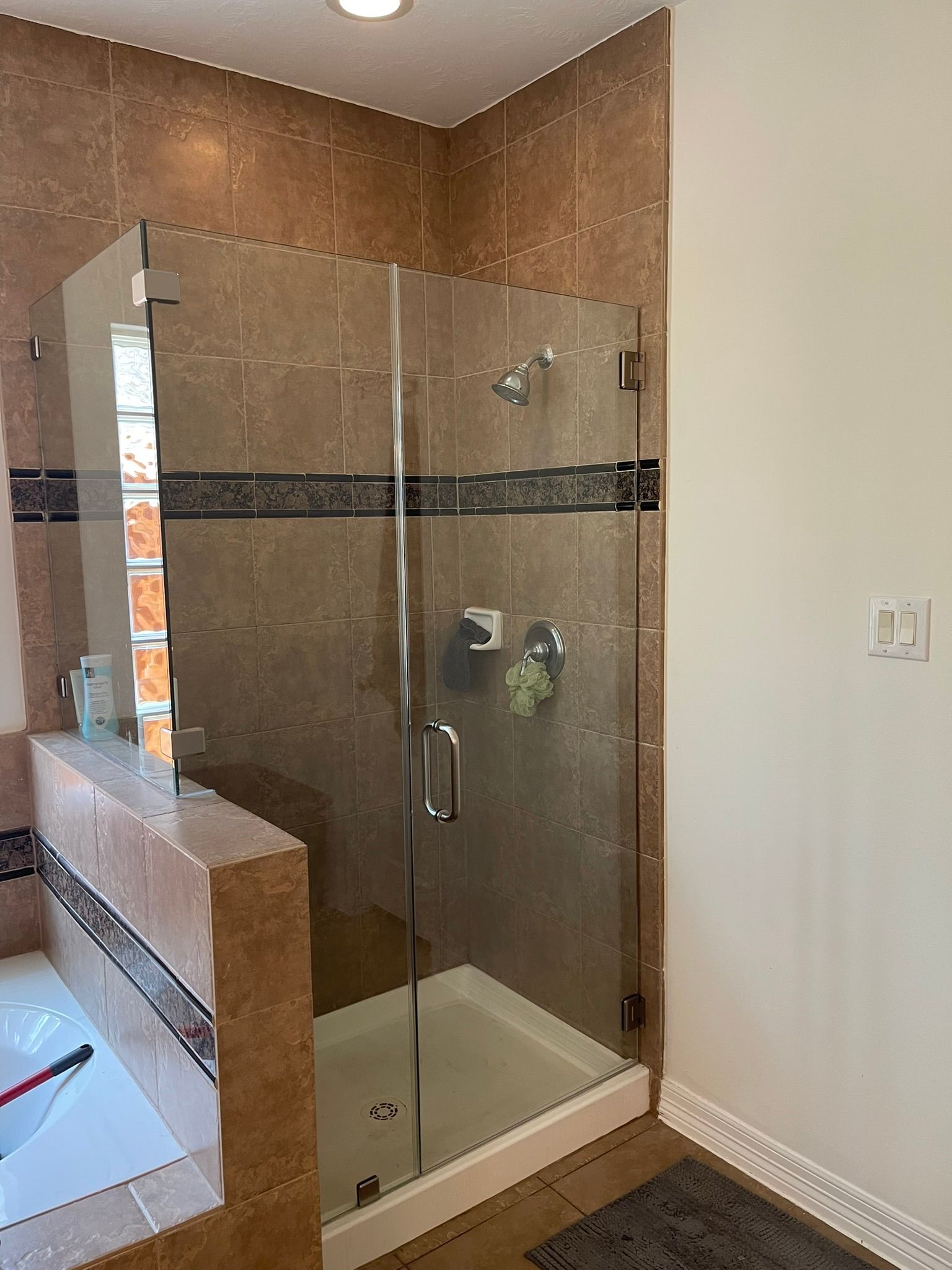 A glass-enclosed shower with brown, textured tile walls, featuring a decorative border and silver fixtures.