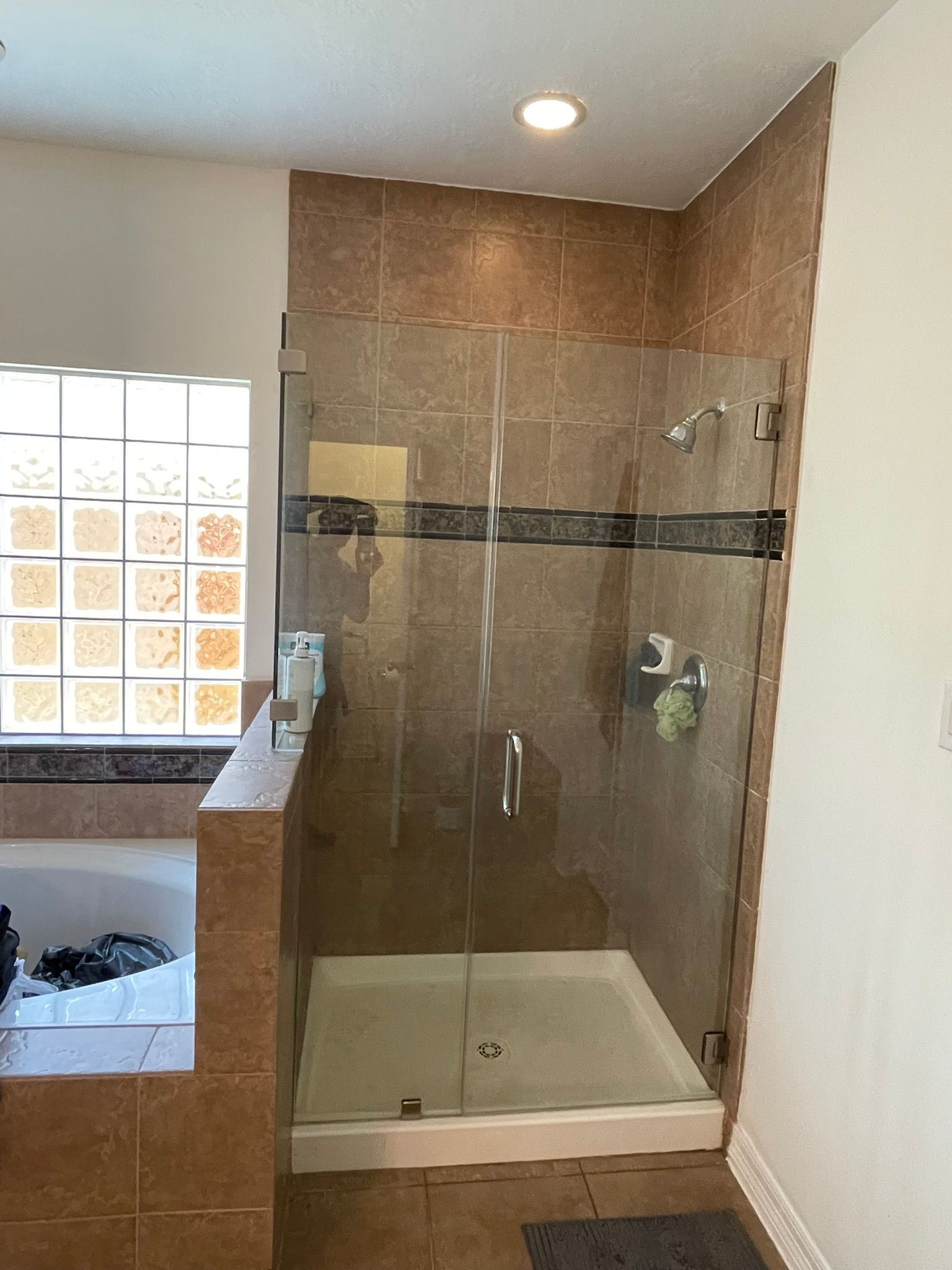 A walk-in shower with brown tile walls, a glass door, and a decorative tile accent strip next to a corner bathtub.