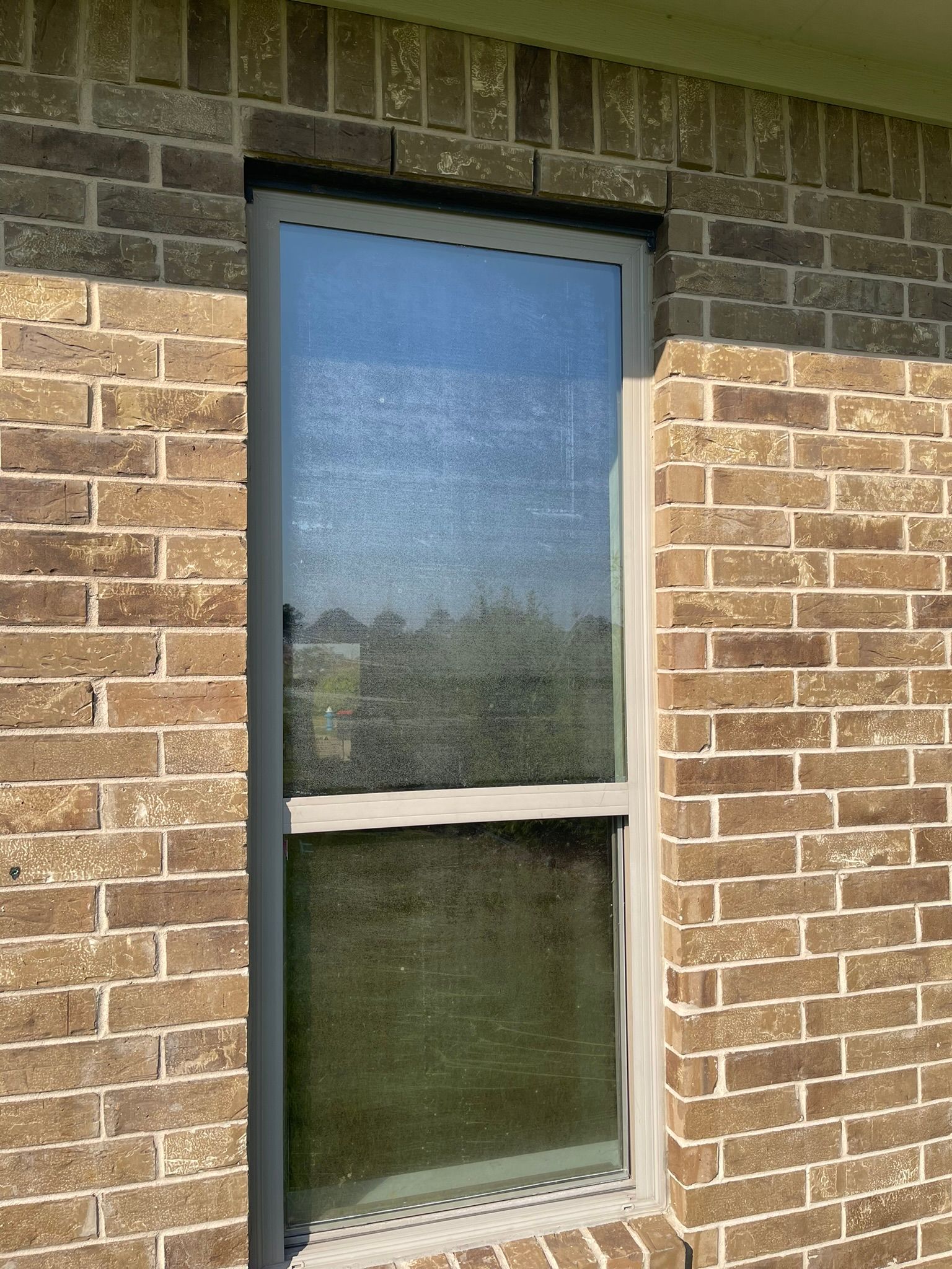 A vertical rectangular window with a grey frame set into a brown brick wall.