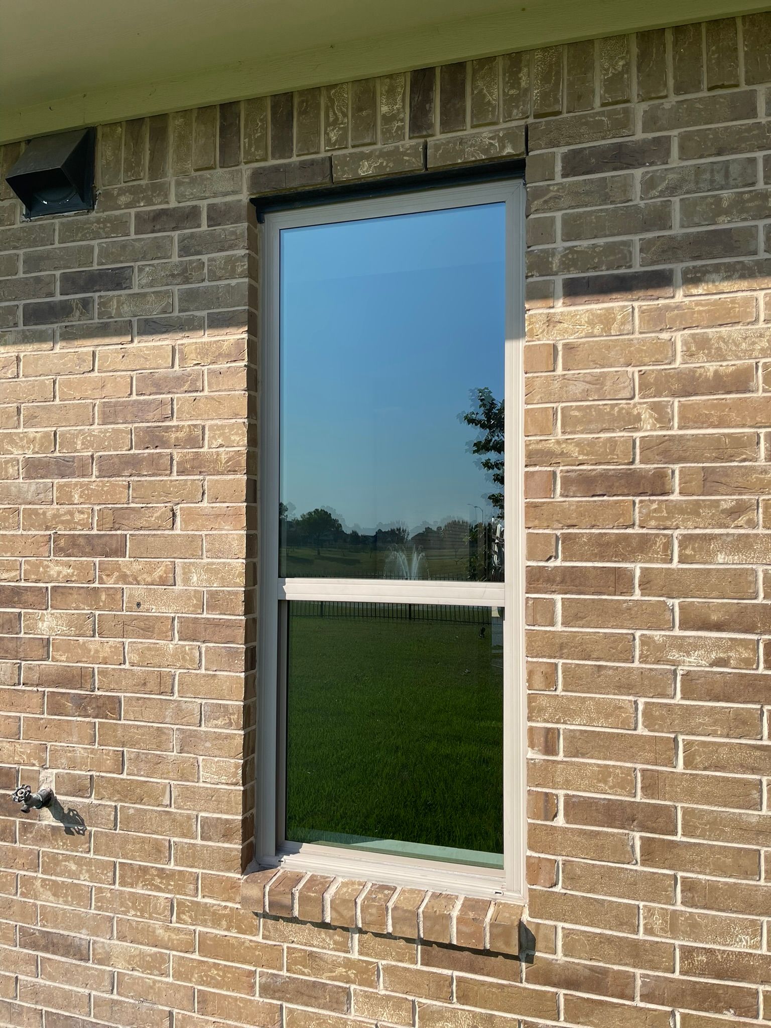 A tall, rectangular window with a reflective pane set into a brown brick wall.