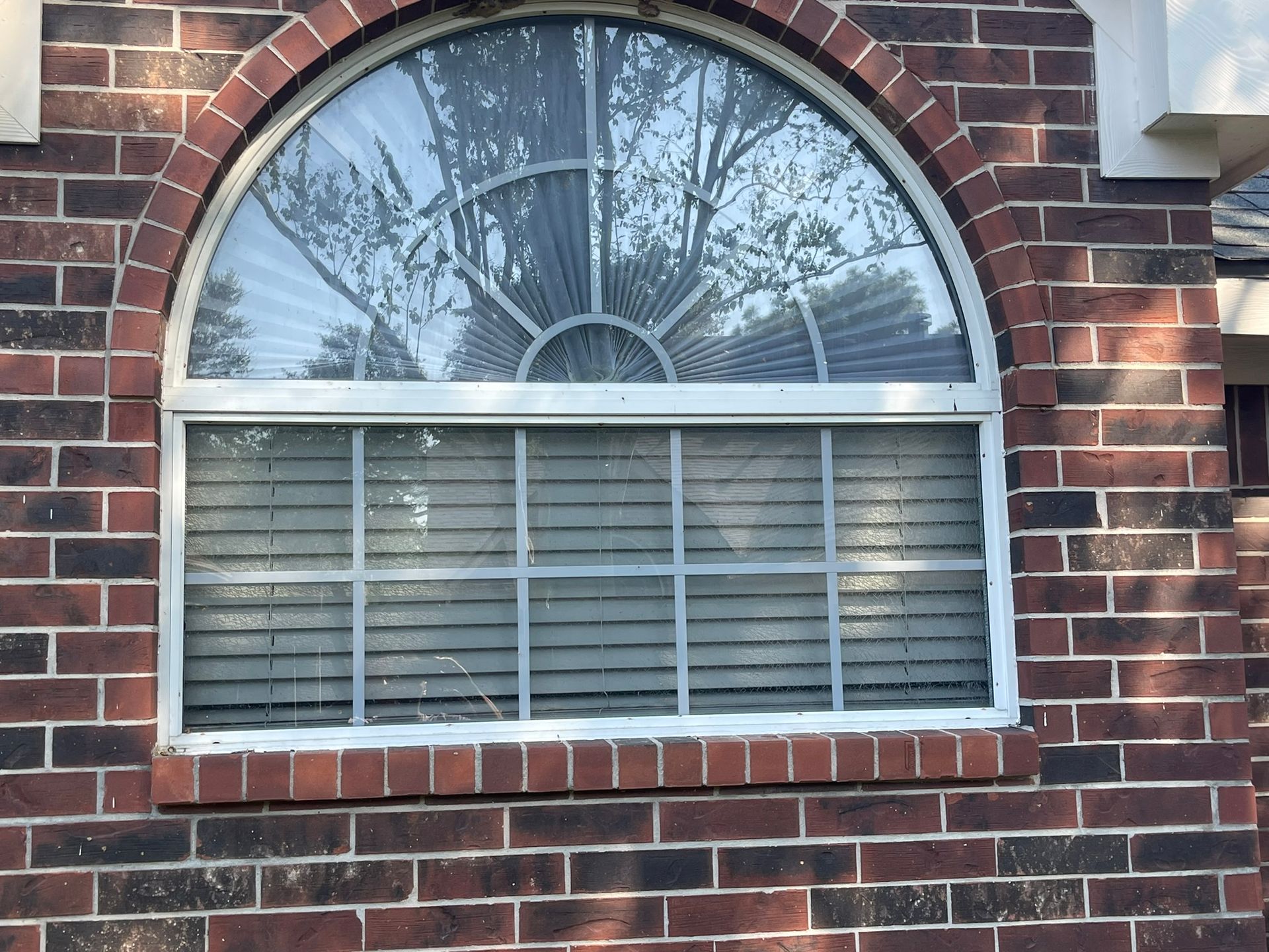 A rectangular window topped by a semi-circular sunburst pane, set into a red brick wall.