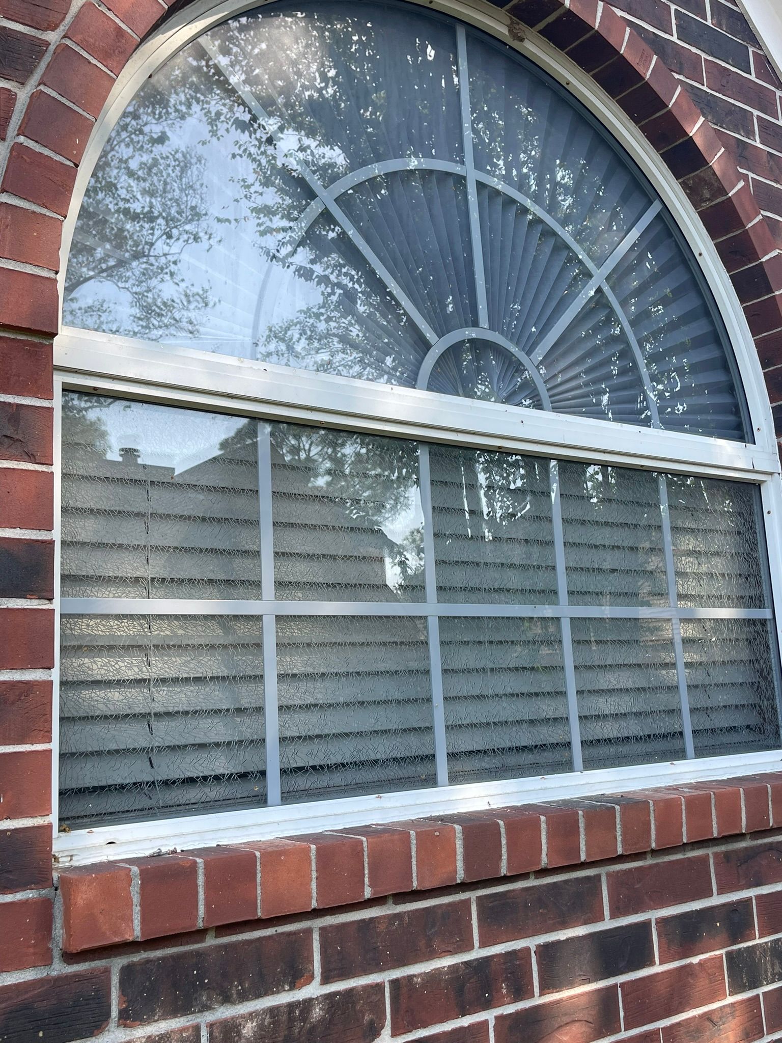 A white-framed arched window with a grid pattern, set into a dark red brick wall.