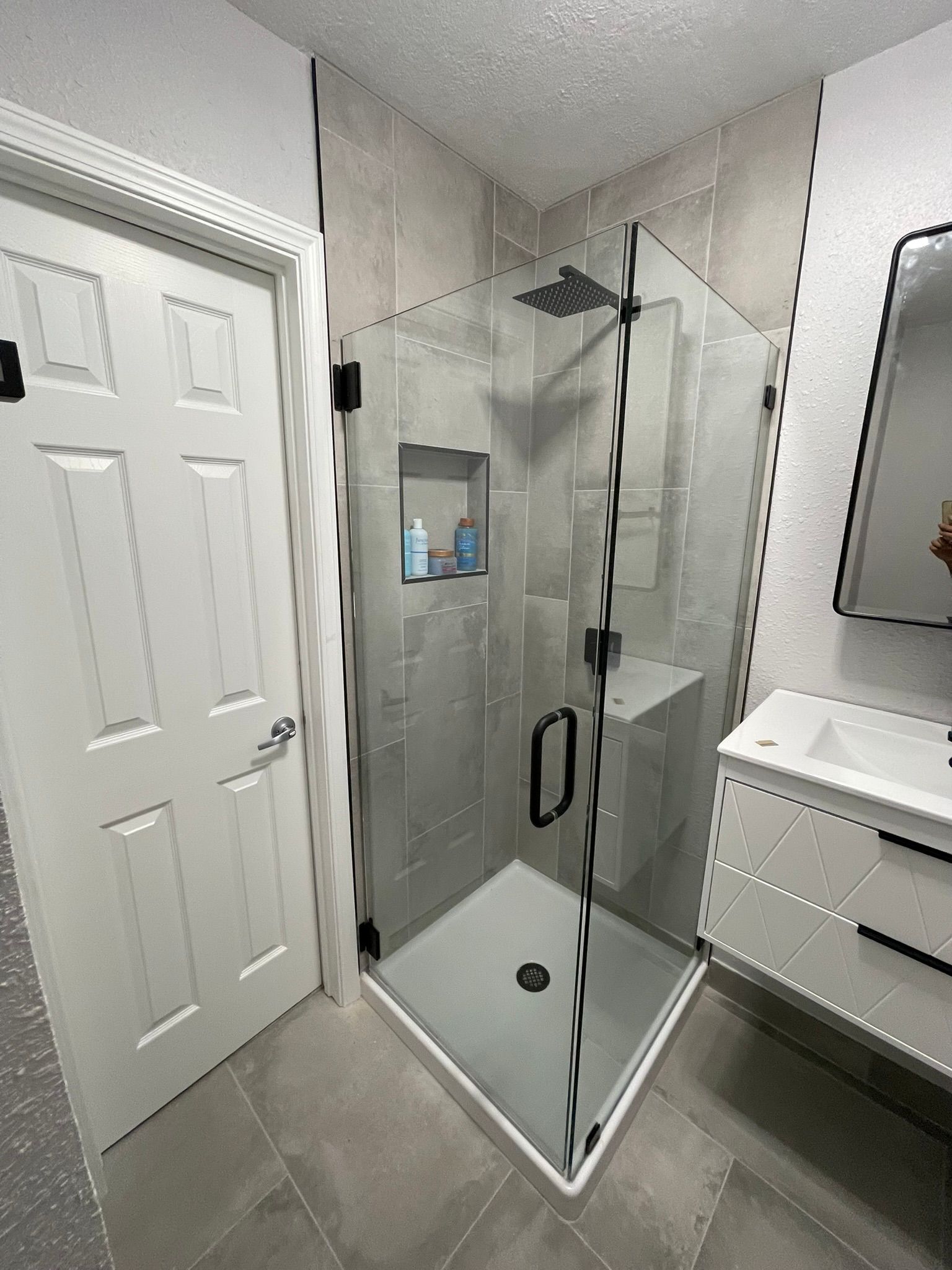 A bathroom corner featuring a glass-enclosed shower with black fixtures next to a white door and a modern vanity.