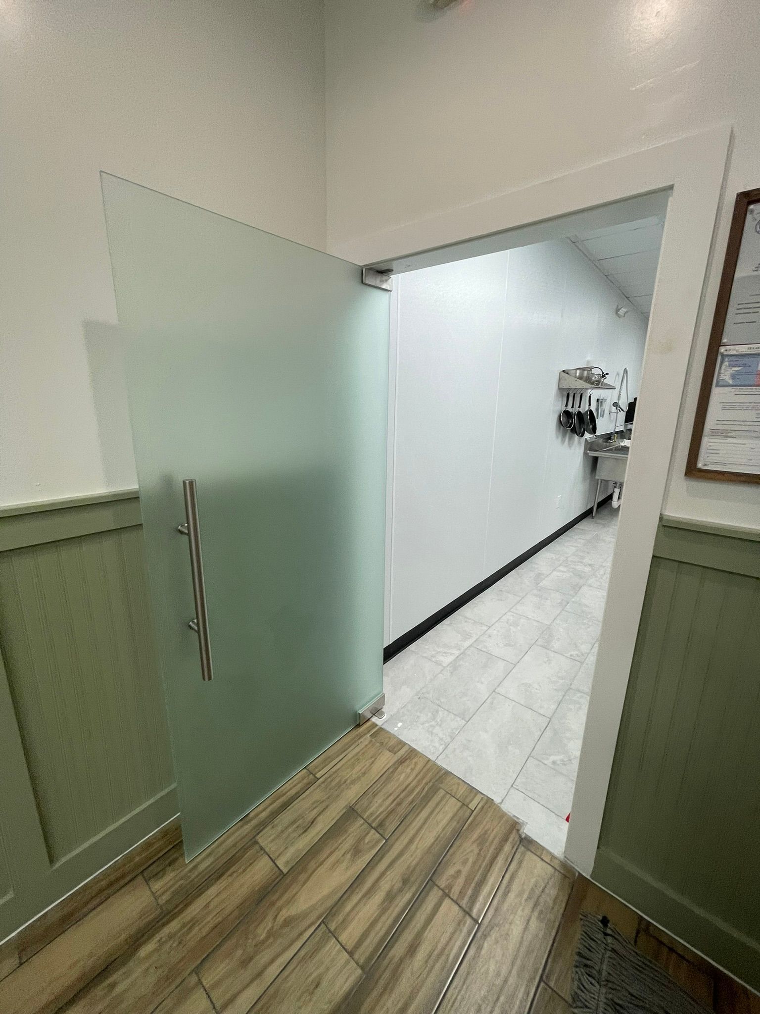 A frosted glass door stands slightly open, revealing a tiled hallway leading to a kitchen area with stainless steel.