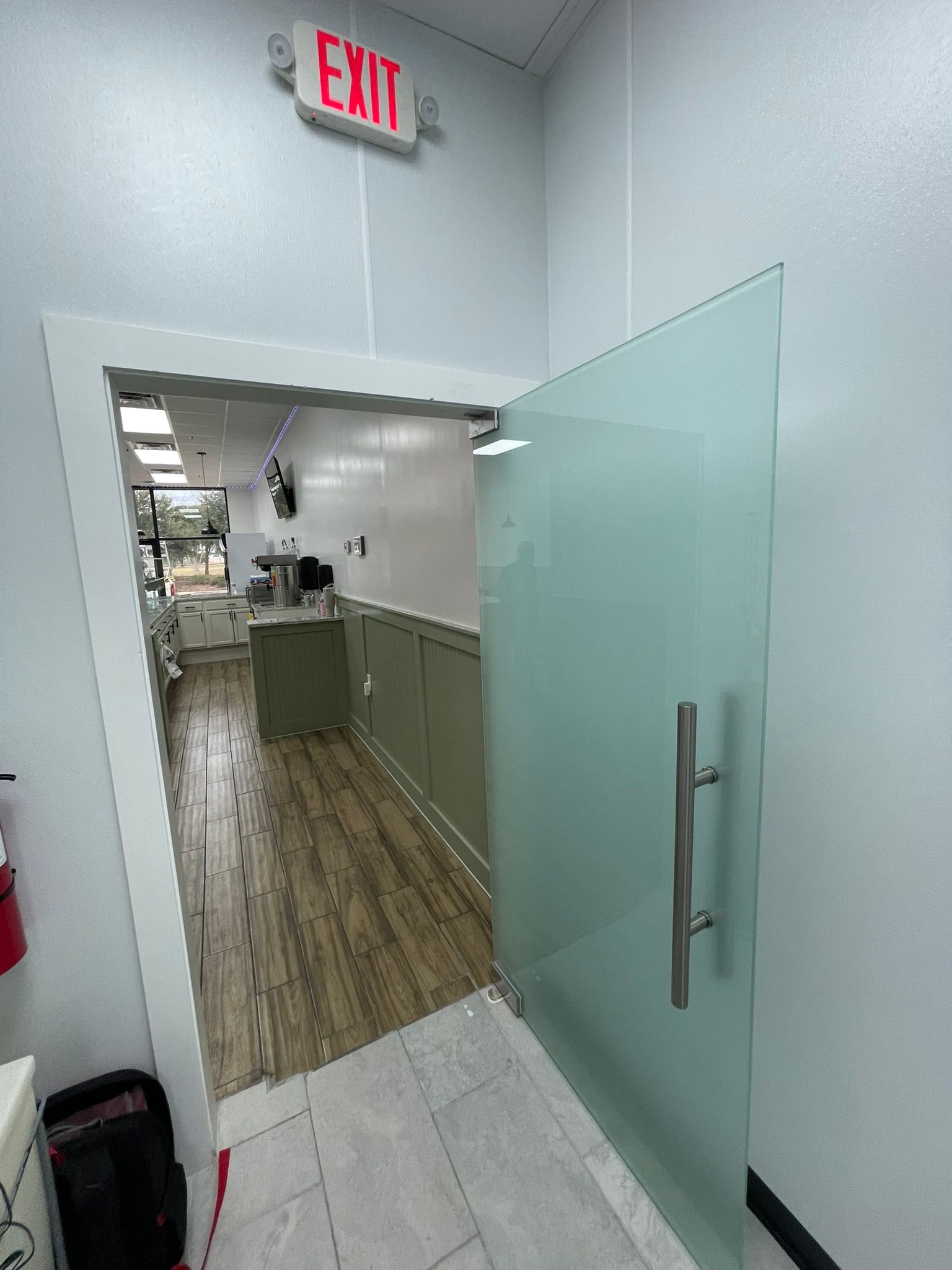 A frosted glass door stands slightly open, revealing a view into a bright room with light wood flooring and cabinets.